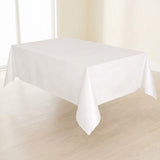 A plain white rectangular tablecloth draped over a table in a bright indoor room with light wood flooring and cream walls.