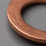 A close-up of a copper washer or gasket ring on a dark gray textured surface.