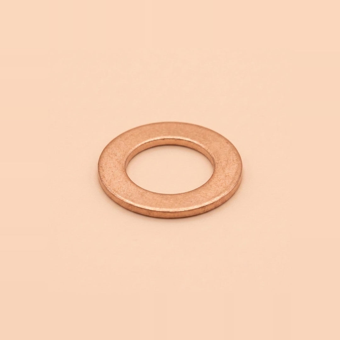 A single flat metal washer with a warm copper or rose-gold metallic finish, centered on a solid, warm peach-beige background.
