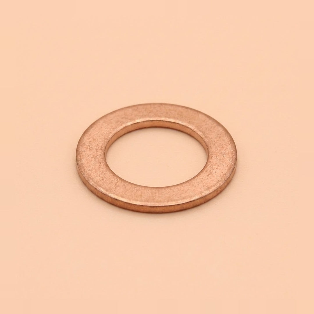 A single flat metal washer with a warm copper or rose-gold metallic finish, centered on a solid peach-beige background.