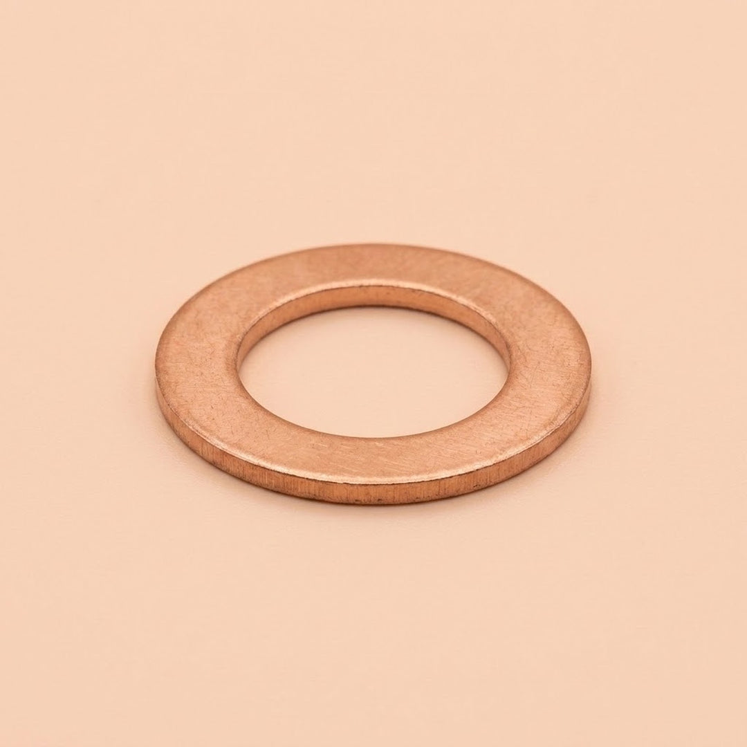 A single flat metal washer with a warm copper or rose-gold metallic finish, centered on a solid, warm beige background.