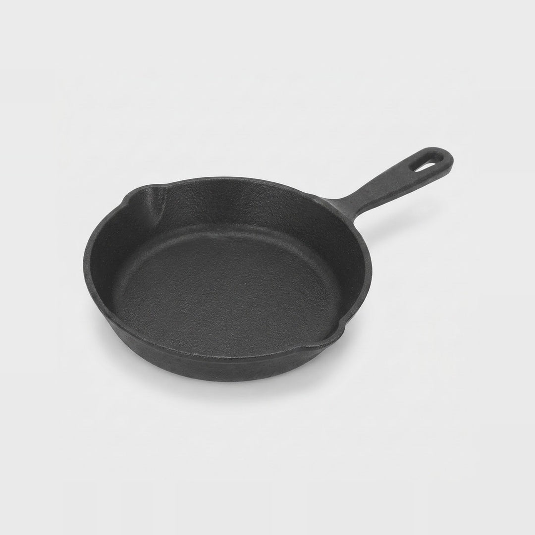 A classic black cast iron skillet with a single loop handle, photographed on a clean, light gray studio background.