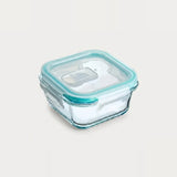 A square glass food storage container with a clear lid and a light aqua silicone seal, shown on a plain light beige background.