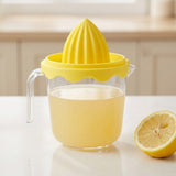 A yellow citrus juicer with a clear glass pitcher filled with lemon juice, set on a white countertop with a halved lemon beside it.