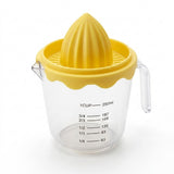A clear plastic measuring cup with a yellow citrus juicer cone and matching yellow rim, shown on a white background. The cup has black measurement markings for cups and milliliters.