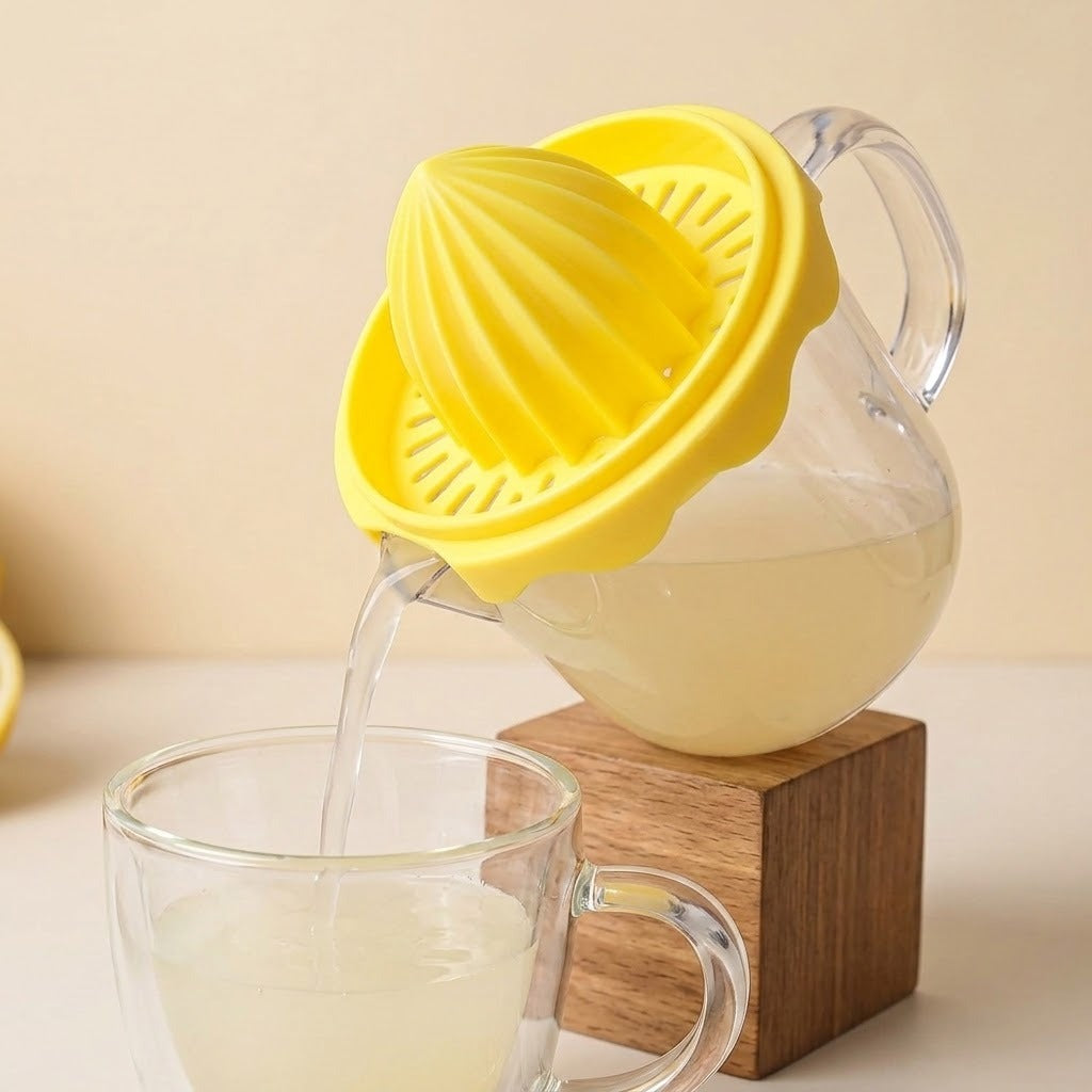 A yellow citrus juicer attachment with a clear glass pitcher, shown pouring juice into a glass cup while resting on a wooden block against a warm beige background.