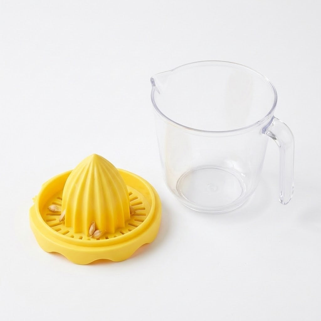Detached yellow citrus reamer with seeds caught in its slotted tray sits beside an empty clear handled cup on white.