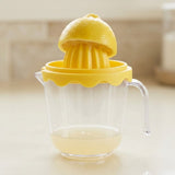 Lemon half rests on a yellow citrus reamer above a clear handled cup containing a little juice on a kitchen counter.