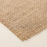 A close-up of a natural burlap fabric swatch showing its coarse woven texture and frayed edges, laid flat on a light beige background.