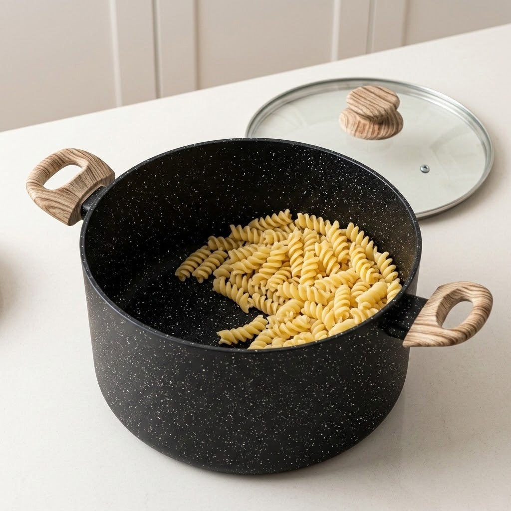 A black speckled non-stick pot with light wood handles sits on a white countertop, filled with rotini pasta, with a matching glass lid resting behind it.