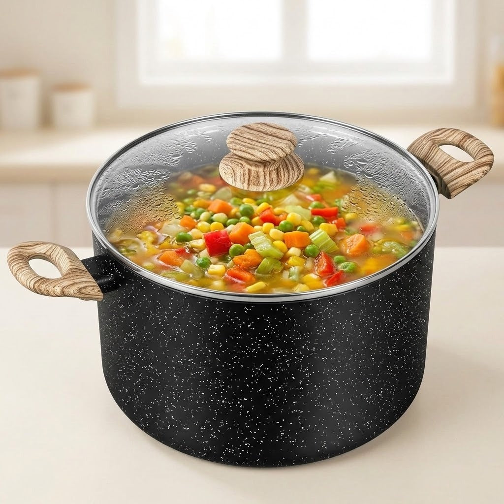 A black speckled pot with a clear glass lid and light wood handles, filled with a colorful vegetable stew, set on a kitchen counter with a blurred background.