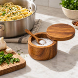 Acacia wood salt cellar sits open beside a pasta pot for quick seasoning while cooking.