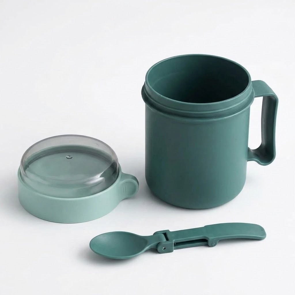 Green plastic soup mug with detached clear-topped lid and unfolded green spoon arranged on a white background.