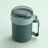 A dark green insulated mug with a matching dark green handle and a translucent dark gray lid, shown on a light green background.
