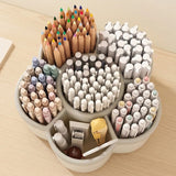A circular, multi-compartment desk organizer filled with stationery items, including colored pencils, pens, markers, a yellow pencil, and small accessories, set on a light wood desk.