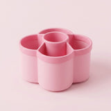 A pink flower-shaped multi-compartment cup organizer with four outer cups and one central cup, shown on a solid pale pink background.