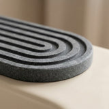 A close-up of a dark gray textured mat with concentric curved ridges, resting on a smooth beige surface.