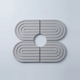 Four light gray oval coasters with concentric rectangular ridges and a circular cutout in the center, arranged in a 2x2 layout on a light gray background.