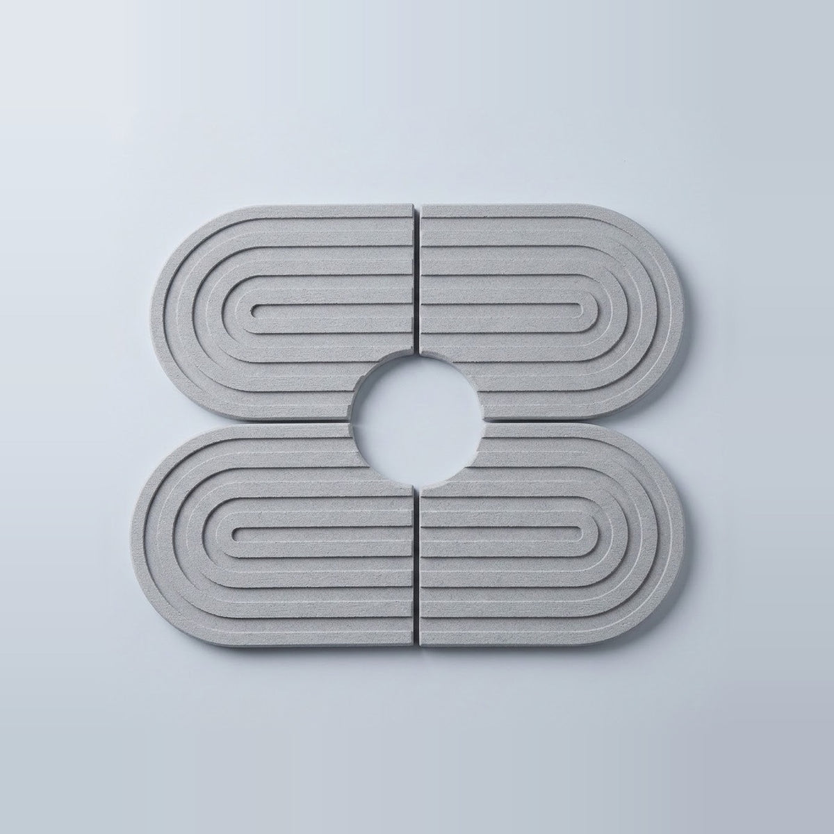 Four light gray oval coasters with concentric rectangular ridges and a circular cutout in the center, arranged in a 2x2 layout on a light gray background.