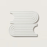 Two white, book-shaped decorative wall art pieces with concentric ridged lines, displayed on a light beige background.