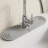 Light gray grooved diatomite mat forms two halves around a chrome faucet against a cream tiled backsplash.