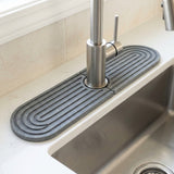 Dark gray two-piece diatomite mat with curved grooves surrounds a brushed metal faucet beside a stainless steel sink.