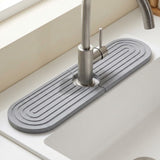 Medium gray grooved diatomite mat surrounds a brushed metal faucet on a white sink ledge beneath a window.