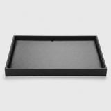 A minimalist black rectangular tray with a brushed metal interior, photographed from a high angle on a light gray background.