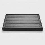 A rectangular black tray with a slatted top and raised rim, photographed from above on a clean light gray background.