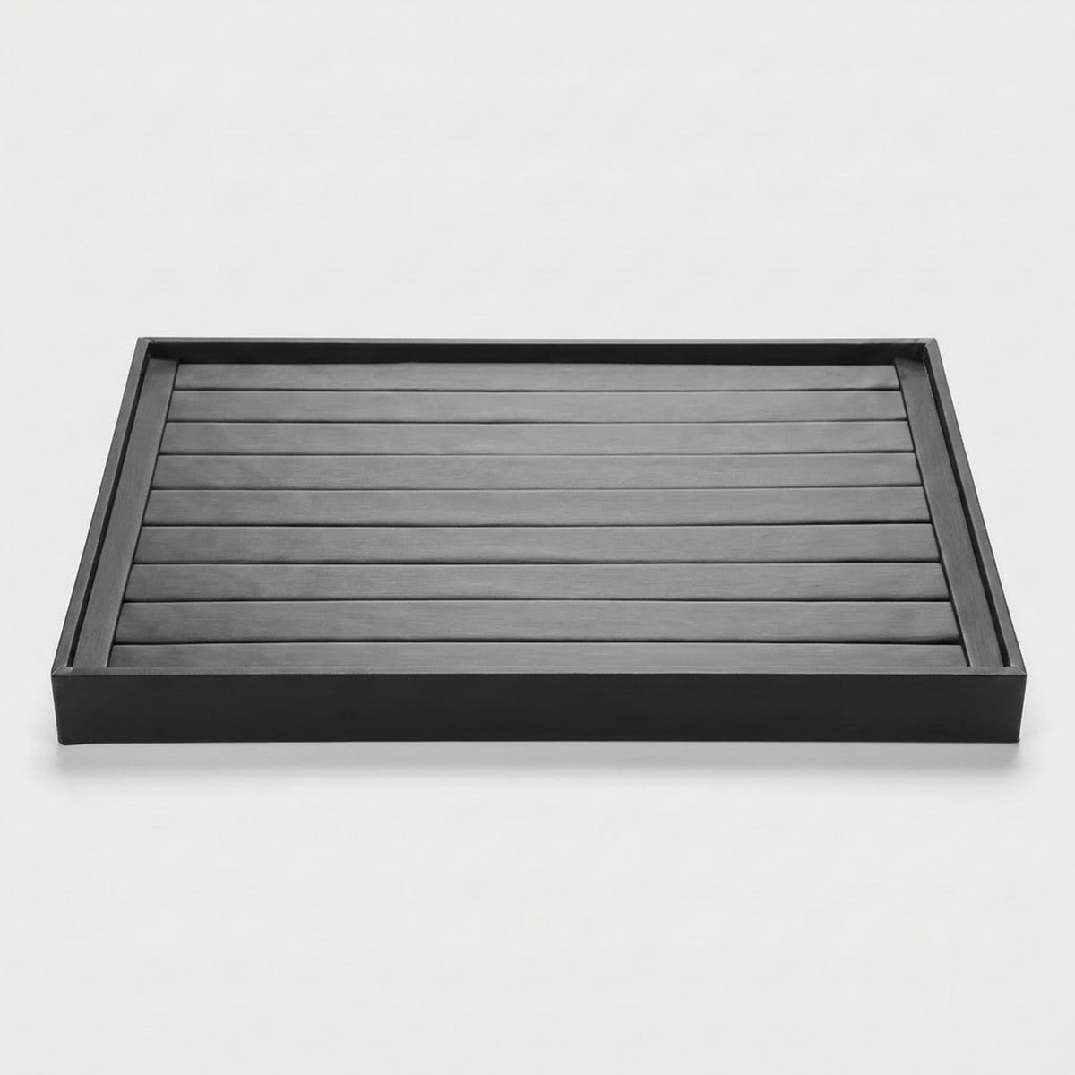 A rectangular black tray with a slatted top and raised rim, photographed from above on a clean light gray background.
