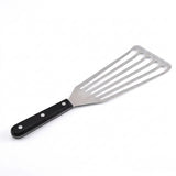 A silver slotted spatula with a black handle and three silver rivets lies diagonally against a white background.