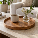 Round wooden serving tray gathers a cup and small vase neatly on a living room coffee table.