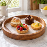 Round wooden serving tray presents small pastries in a bright kitchen, with its raised edge visible.