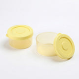 Two small round plastic storage containers with translucent pale yellow lids on a white background, one closed and one open with its lid leaning against it.