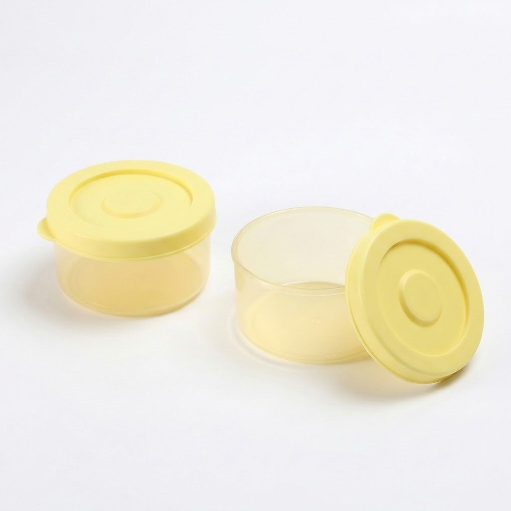 Two small round plastic storage containers with translucent pale yellow lids on a white background, one closed and one open with its lid leaning against it.