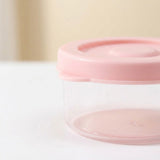 A small clear plastic storage container with a light pink lid, shown on a white surface with a soft beige background.