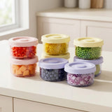 Clear round containers with pink, yellow, and lavender lids hold chopped vegetables and blueberries, arranged in stacks on a white kitchen counter.