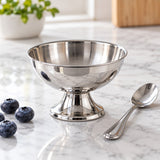 Small short pedestal stainless steel dessert cup sits beside a teaspoon and blueberries.