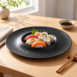 Black melamine serving plate keeps sushi centered in its recessed well at a simple dining table.