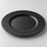 Black melamine dinner plate with a broad textured rim and smooth recessed center on a studio backdrop.