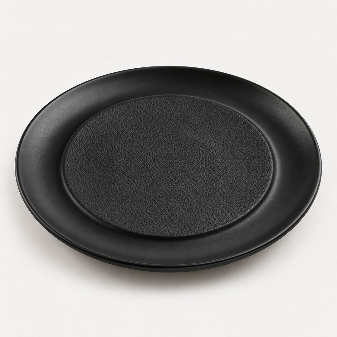 Black raised center melamine plate with a textured middle and smooth outer lip on a light backdrop.