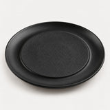Black raised center melamine plate with a textured middle and smooth outer lip on a light backdrop.