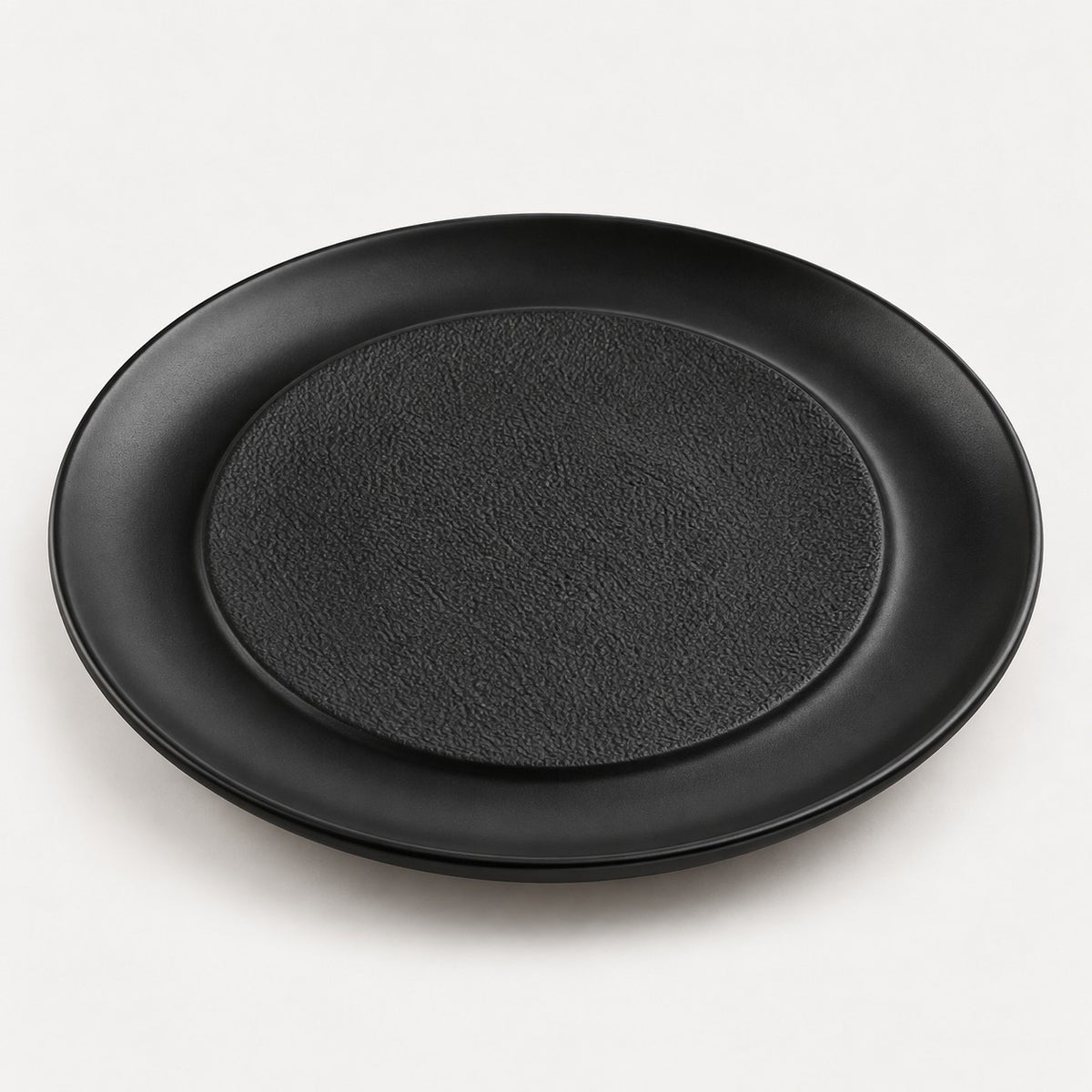 Black raised center melamine plate with a textured middle and smooth outer lip on a light backdrop.