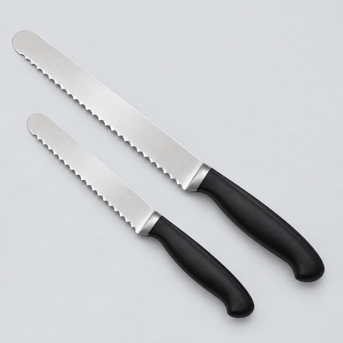 Two stainless steel serrated bread knives, one longer than the other, are shown on a pale backdrop.