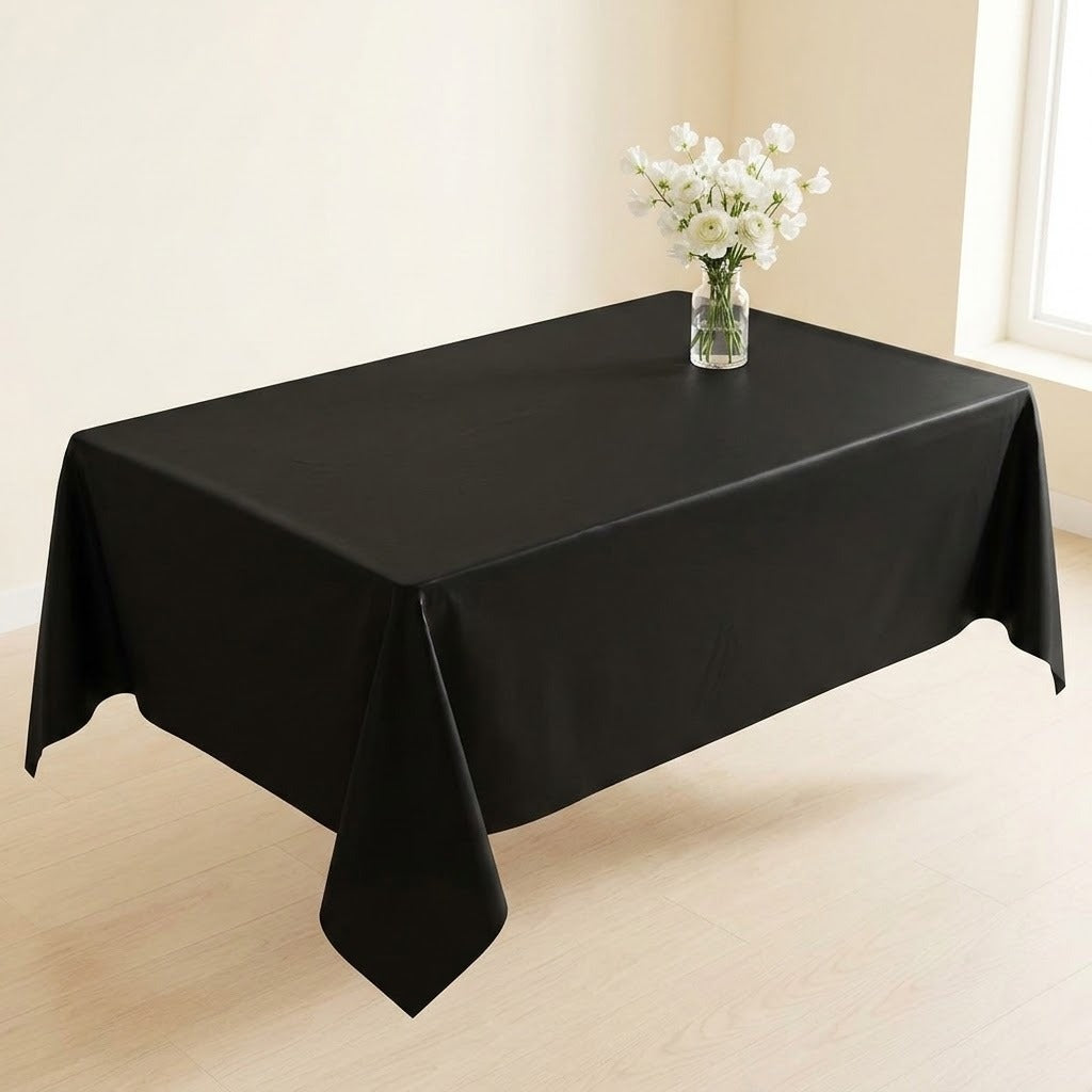 A black rectangular tablecloth draped over a table in a bright room, with a small vase of white flowers placed on top.