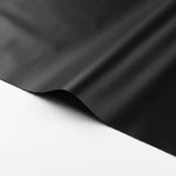 Close-up of a black tablecloth shows a smooth surface, gentle folds and a lifted edge against a white background.