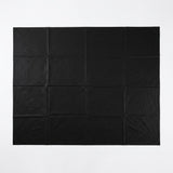 A black square fabric backdrop or sheet with a grid of nine stitched panels, laid flat against a solid white background.