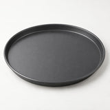 Dark round pizza pan shown alone on a pale background, highlighting its smooth nonstick surface.