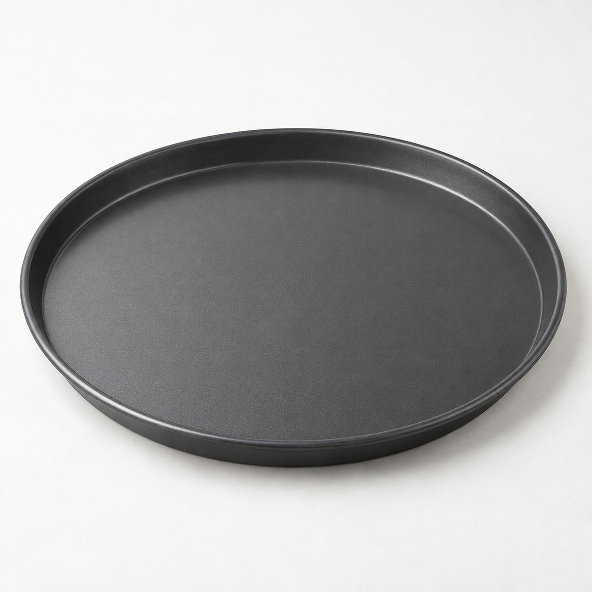Dark round pizza pan shown alone on a pale background, highlighting its smooth nonstick surface.