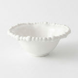 An empty white bowl with a raised beaded rim and small circular foot rests against a pale background.